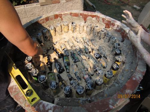 Here we are putting in the base insulation.  Beer bottles separated by small gaps filled with the wood shaving/clay slip mix.  The idea is to provide a solid base with good insulative properties.