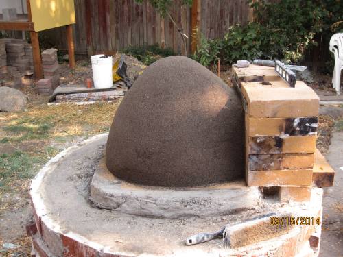 Here we are making a sand castle that will become the void space of our oven.  Instead of going witht the round oven hearth suggested in the book I extended it a wee bit into an eleptical base for a bit more cooking area.  the damp sand was densly packed by whacking with a 2x4. 